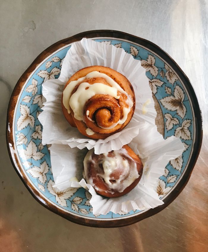 Two fresh cinnamon rolls with icing in a decorative floral dish. Perfect for food photography.