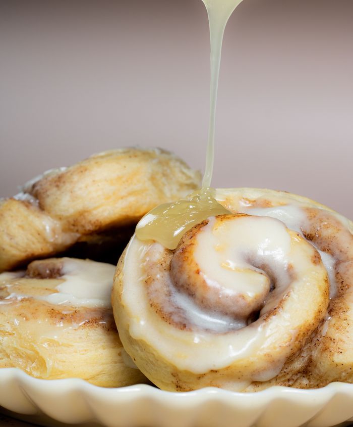 Delicious cinnamon rolls with creamy icing drizzling down, captured in a close-up shot.