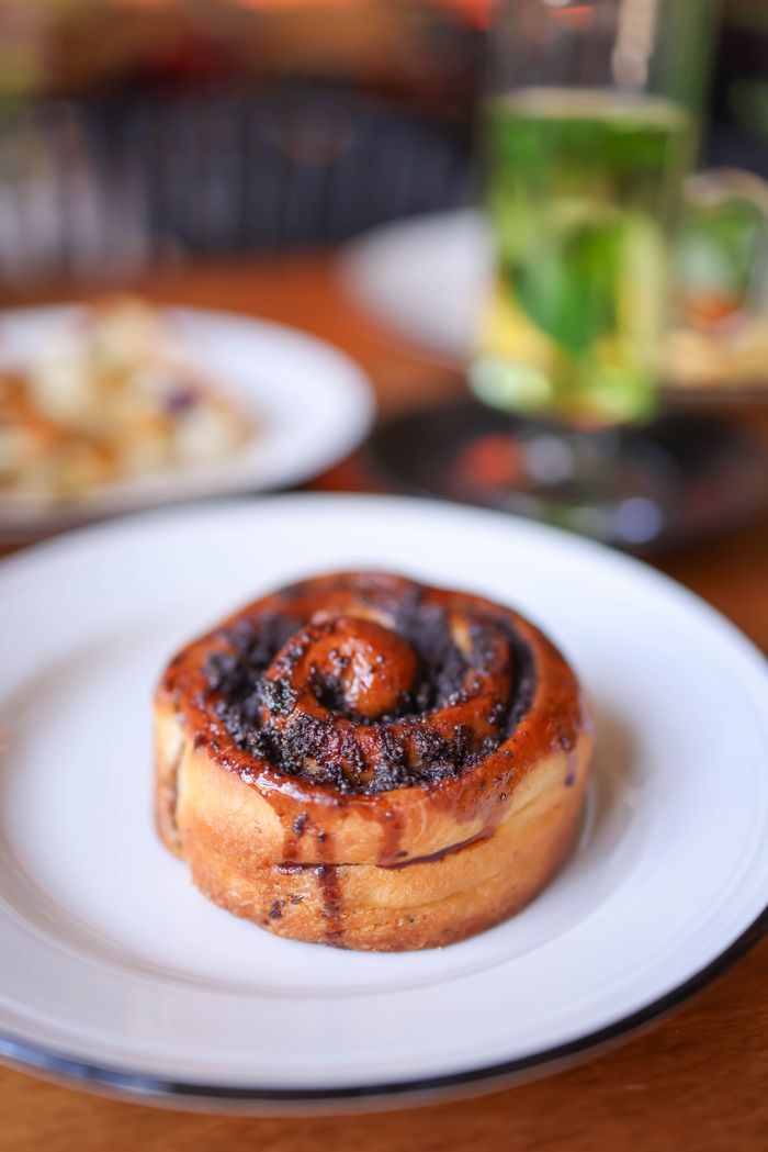 Appetizing cinnamon roll on a white plate with blurred background of tea. Perfect for breakfast themes.